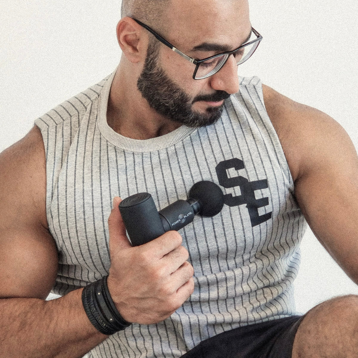 Man using a black Power Plate Mini+ handheld massager on his chest.
