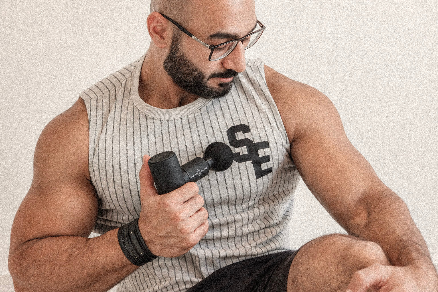 Man using a black Power Plate Mini+ handheld massager on his chest.