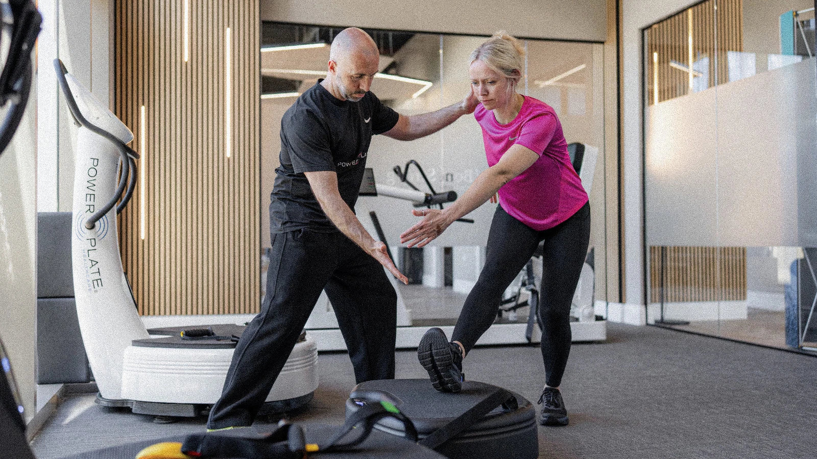 Personal trainer guiding a woman through a stretch using a Power Plate.