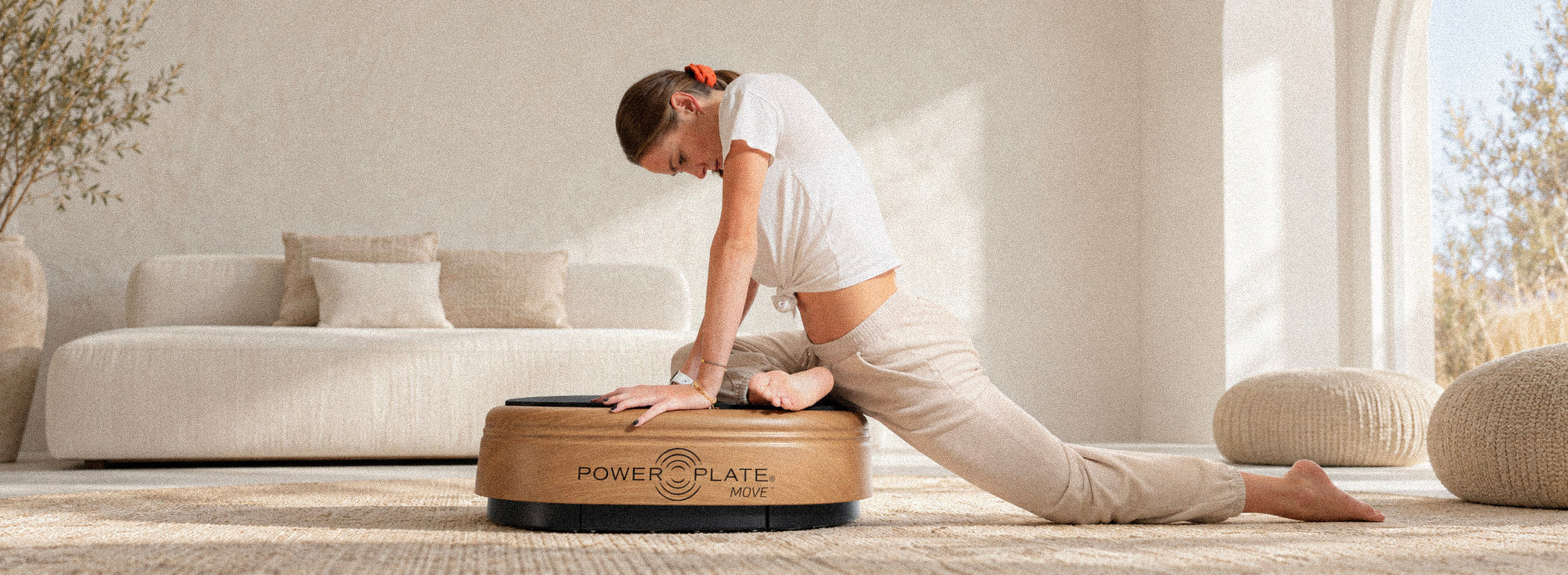 Woman stretching on a wooden Power Plate in a light beige interior.