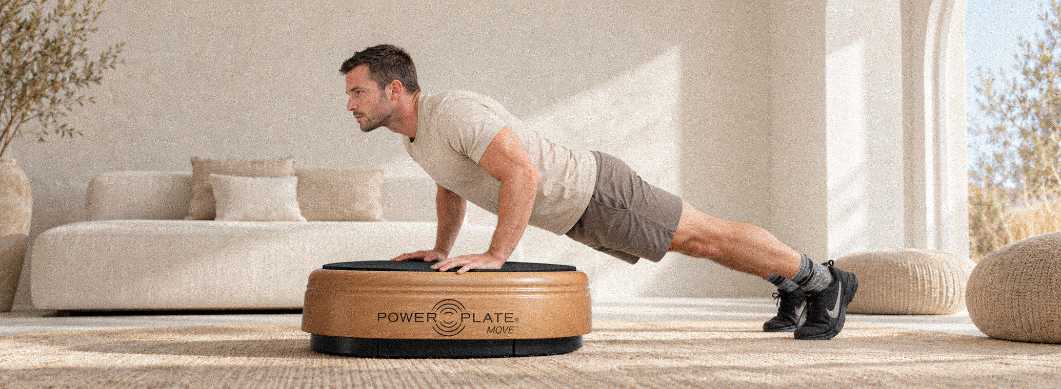 Man exercising on a wooden Power Plate in a light beige interior.