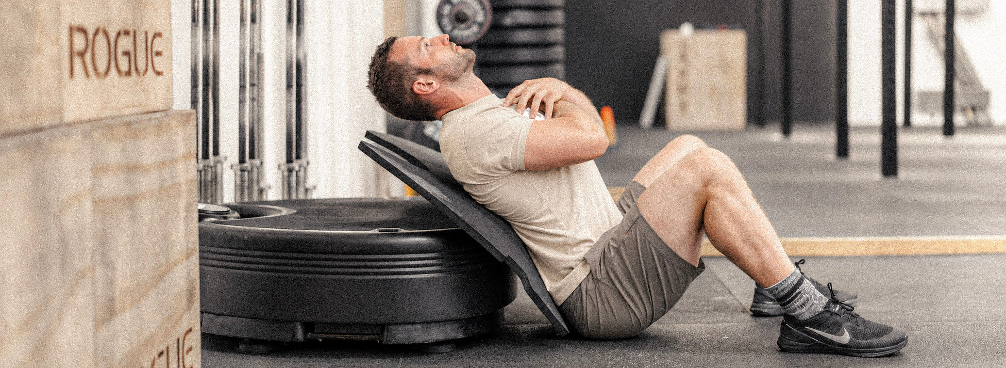 Man in beige clothing performing a supported core exercise beside a black Power Plate.