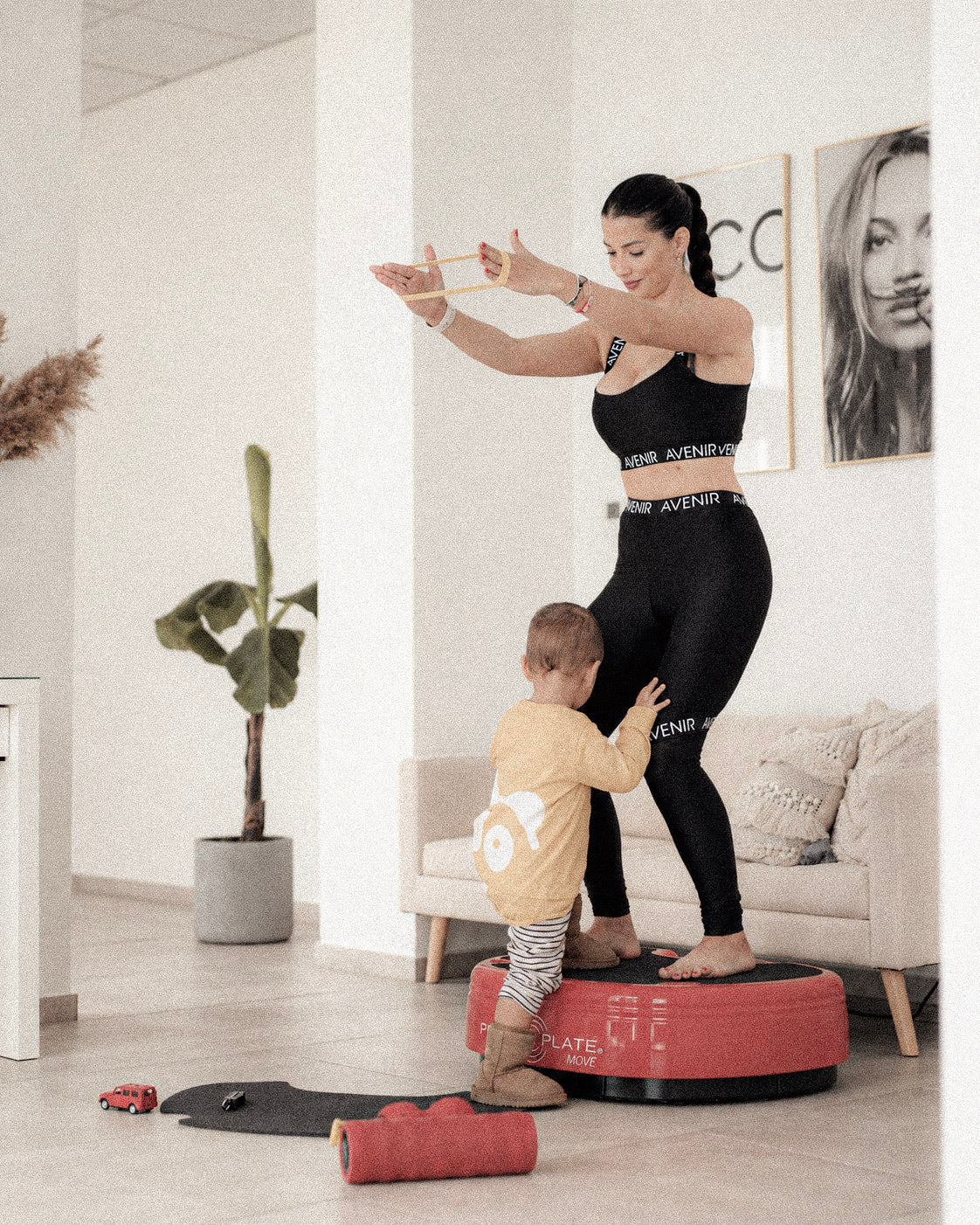 Woman exercising on a Power Plate at home beside her child.