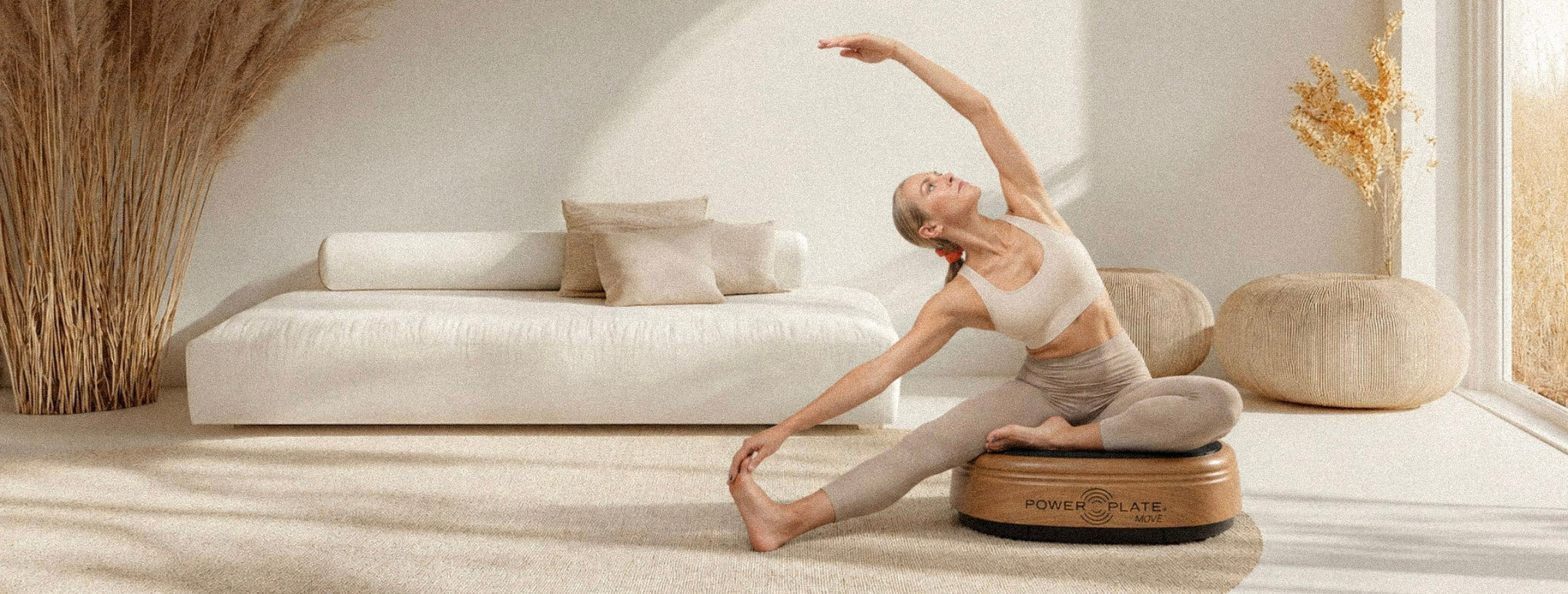 Woman stretching on a wooden Power Plate MOVE in a light beige living room.