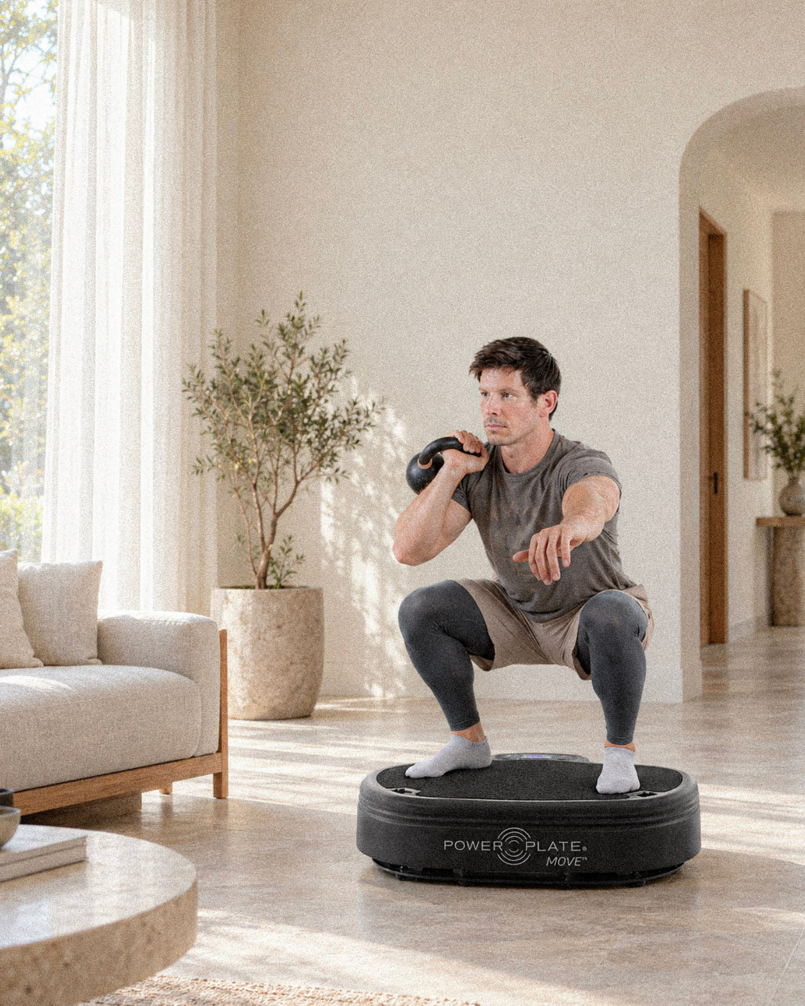 Man performing a kettlebell squat on a Power Plate at home