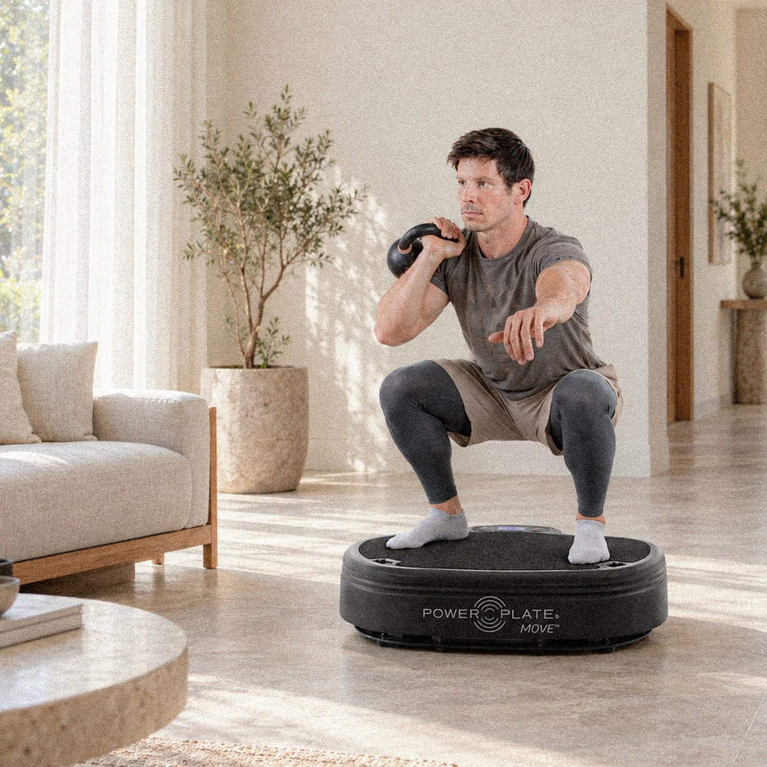 Man performing a kettlebell squat on a Power Plate at home