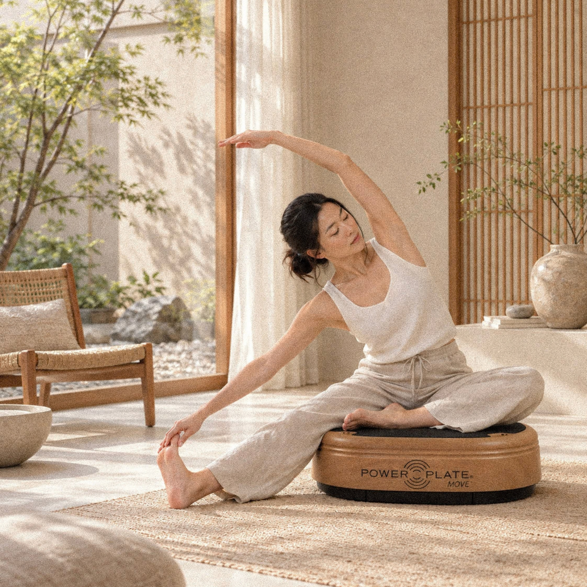 Woman stretching on a wooden Power Plate MOVE in a sunlit natural-toned room.